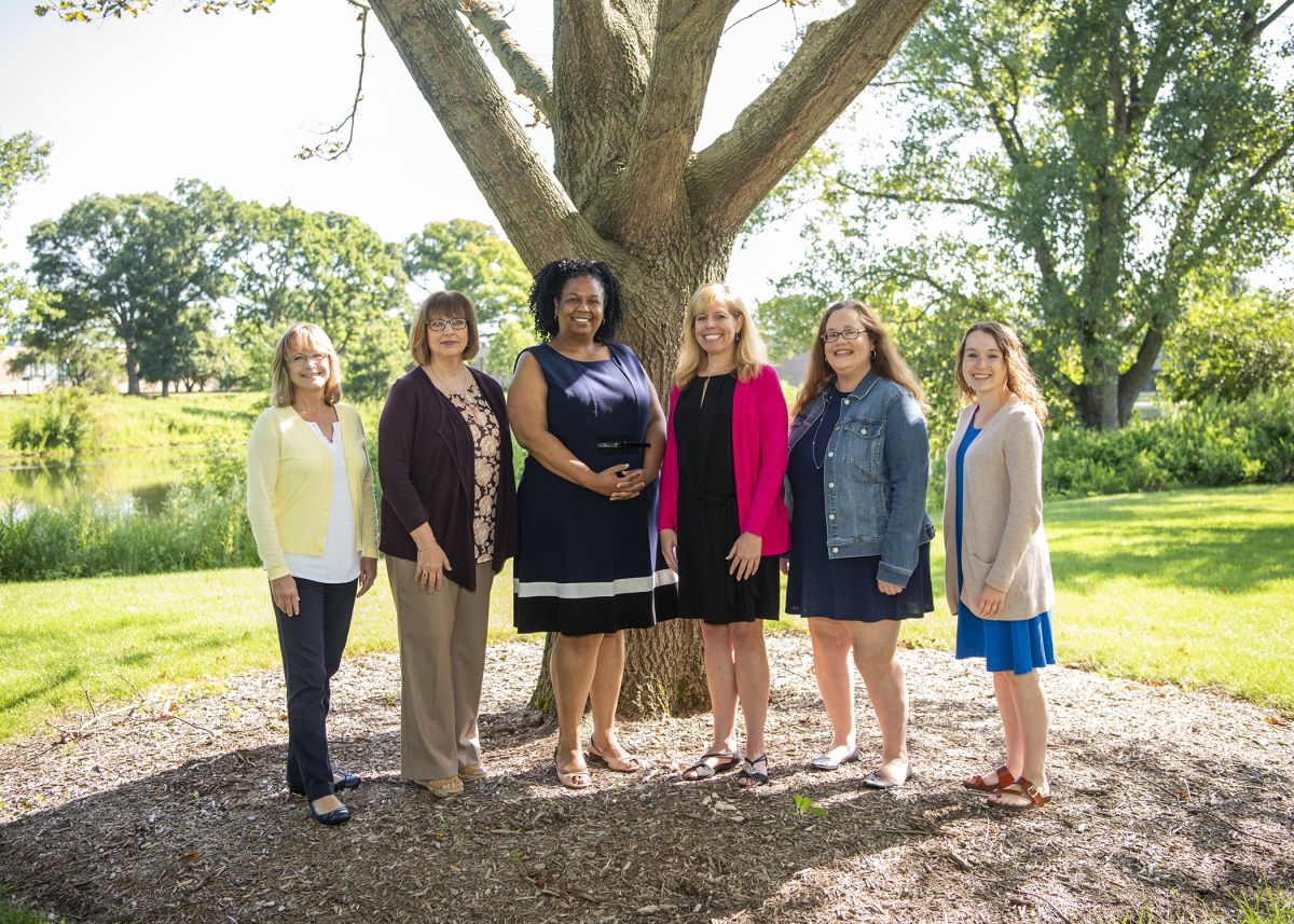 The Learning Outcomes, Curriculum, and Program Development staff standing in front of a tree