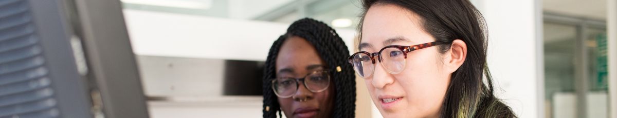 Person sitting at desk next to someone and helping them work on computer 