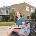 Female student with phone and book outside science building