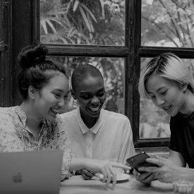 A gray image of a group of ladies sharing digital content using laptop and cell hpone