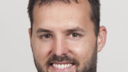 Headshot of Justin smiling with a beard and a white background.